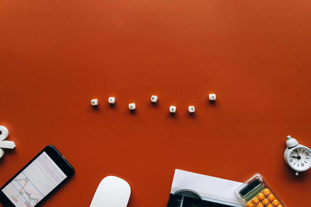 Creative still life with financial tools and the word MARKETS on an orange background.